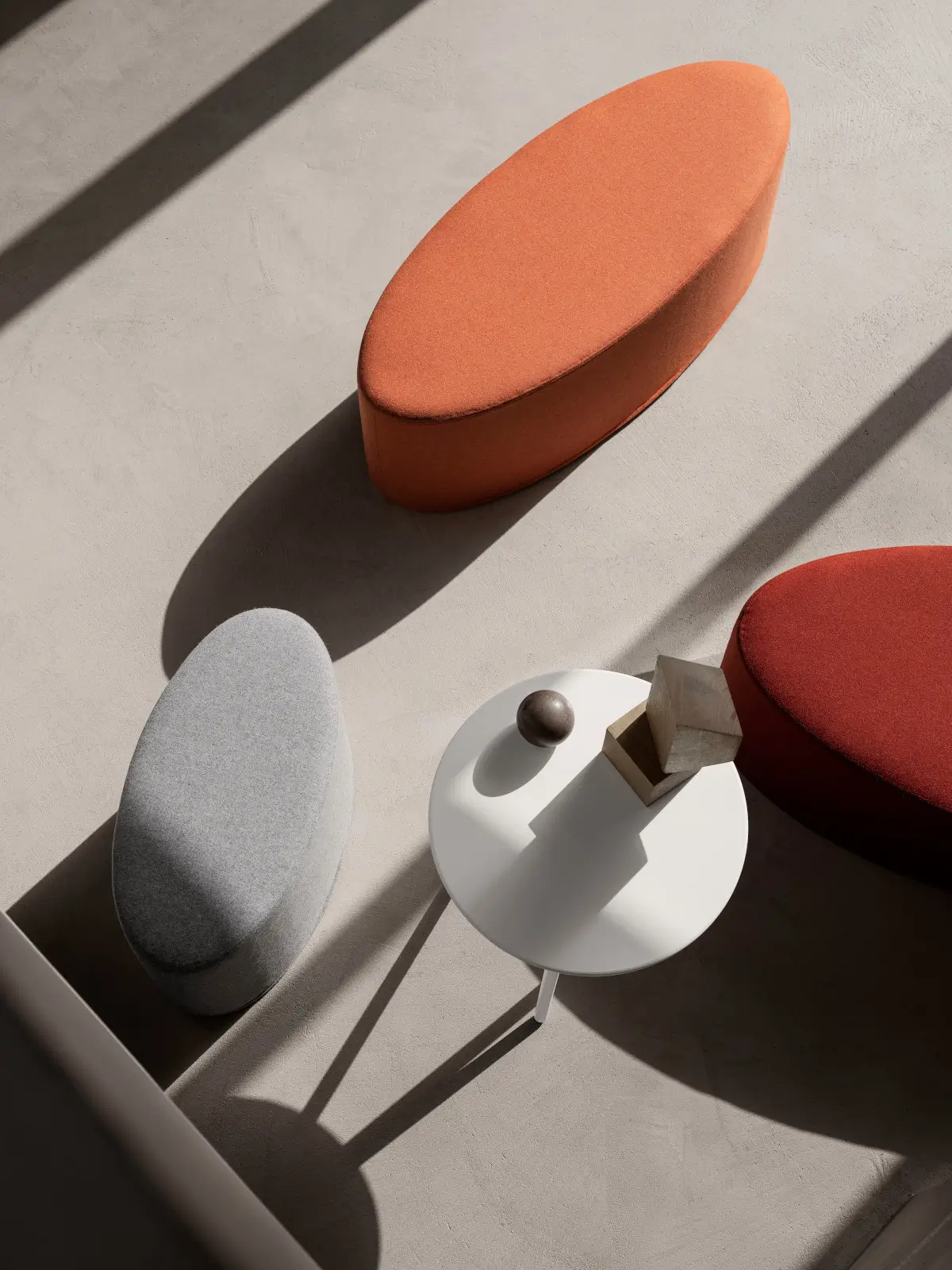 Softline Bon-Bon Hocker Medium in Orange, Hellgrau und Rot aus erhöhter Perspektive rund um einen weißen Beistelltisch in modernem Ambiente.