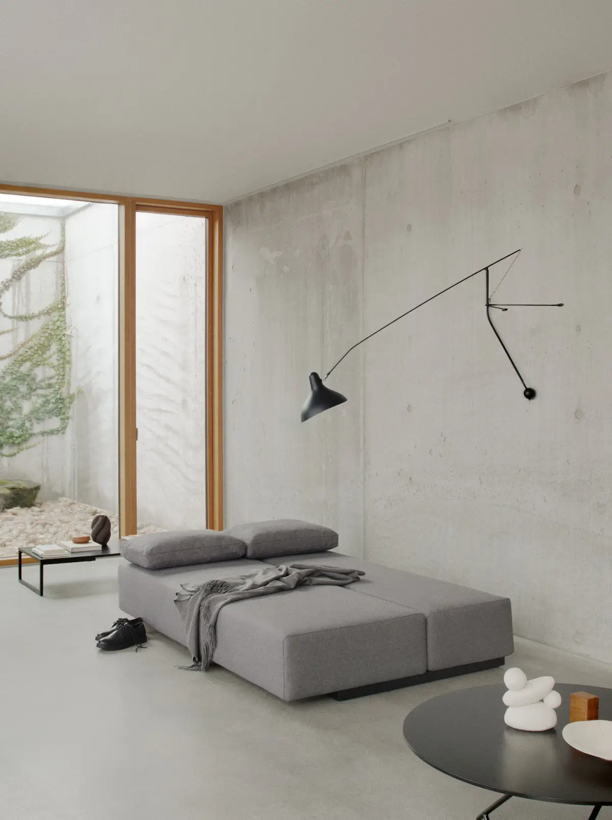 Softline Nevada Sofa 3-Sitzer in Grau als großzügige Liegefläche mit zwei Kopfkissen und Decke in einem modernen Wohnambiente mit Betonwänden.
