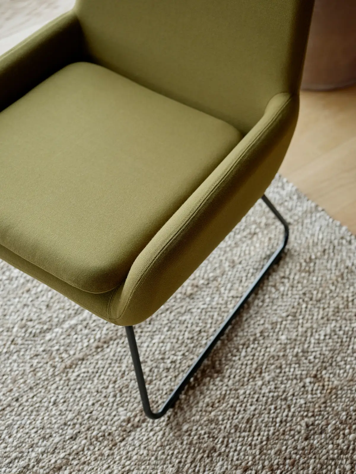 Detailansicht des Softline Coco Sessels in Grün mit gepolsterter Sitzfläche, geschwungenen Armlehnen und schwarzem Kufengestell.