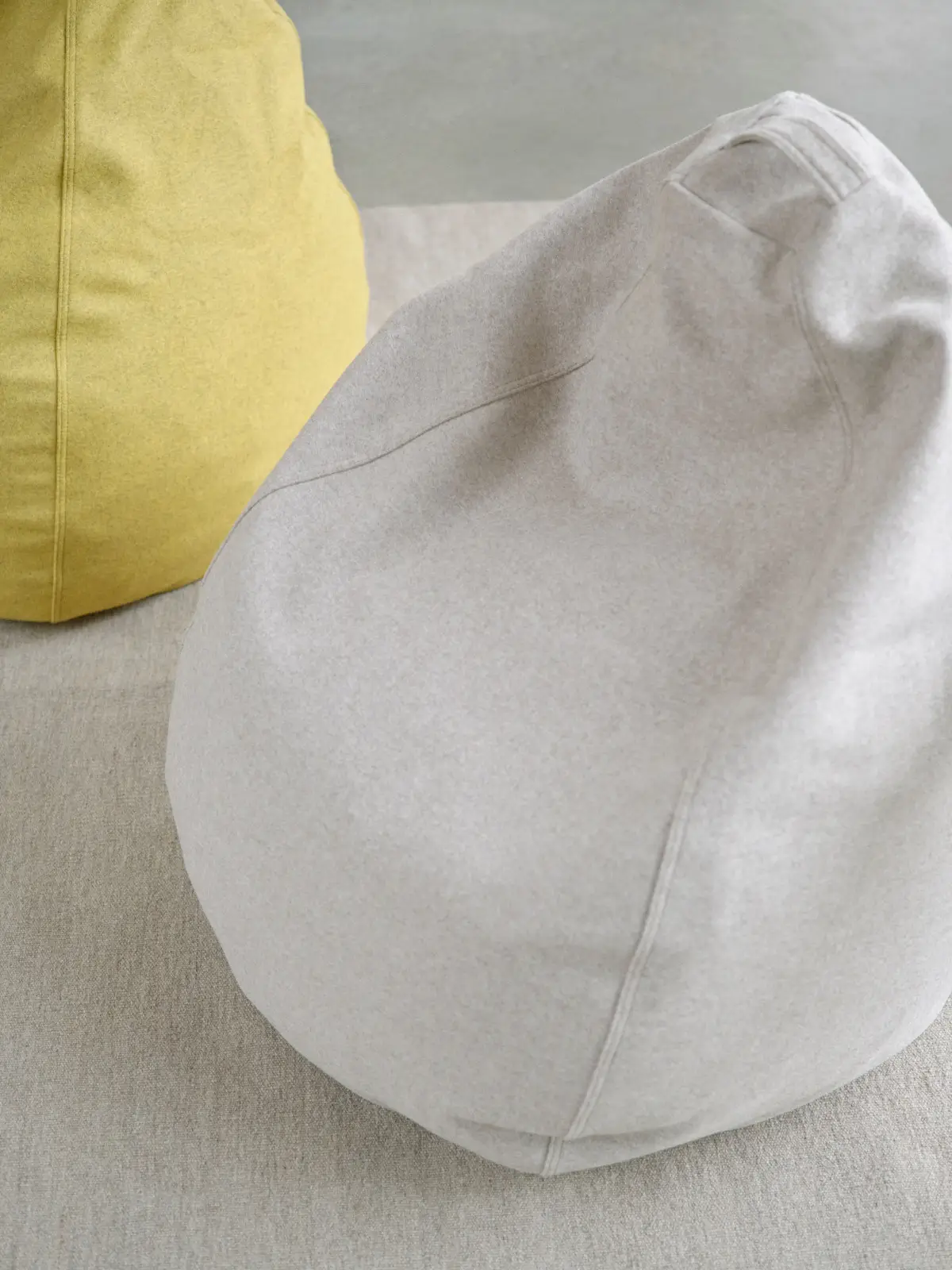 Softline Esprit Sitzsack in Hellgrau aus erhöhter Perspektive mit weicher Form, sichtbaren Nähten und Tragegriff; gelber Sitzsack im Hintergrund.