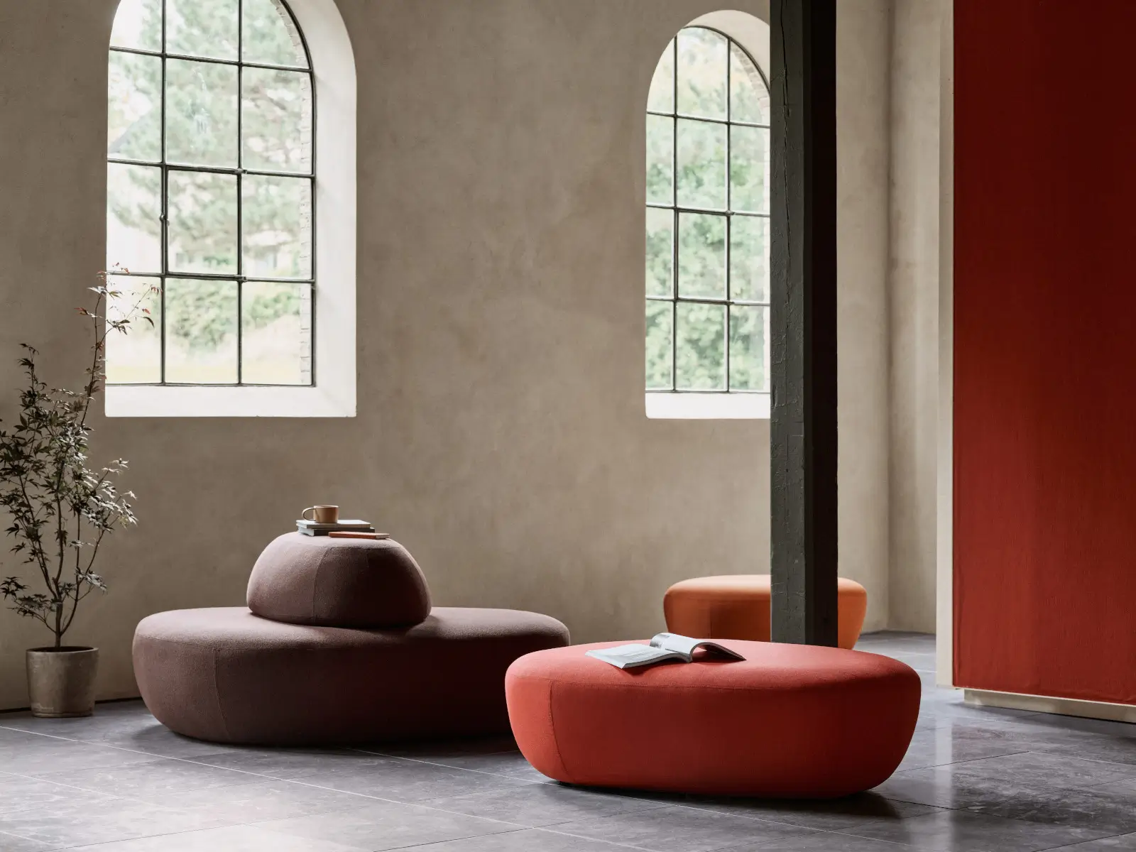 Softline Sisters Hocker Small in Rotbraun in einem stilvollen Wohnambiente mit weiteren organisch geformten Sisters Sitzelementen und hohen Bogenfenstern.