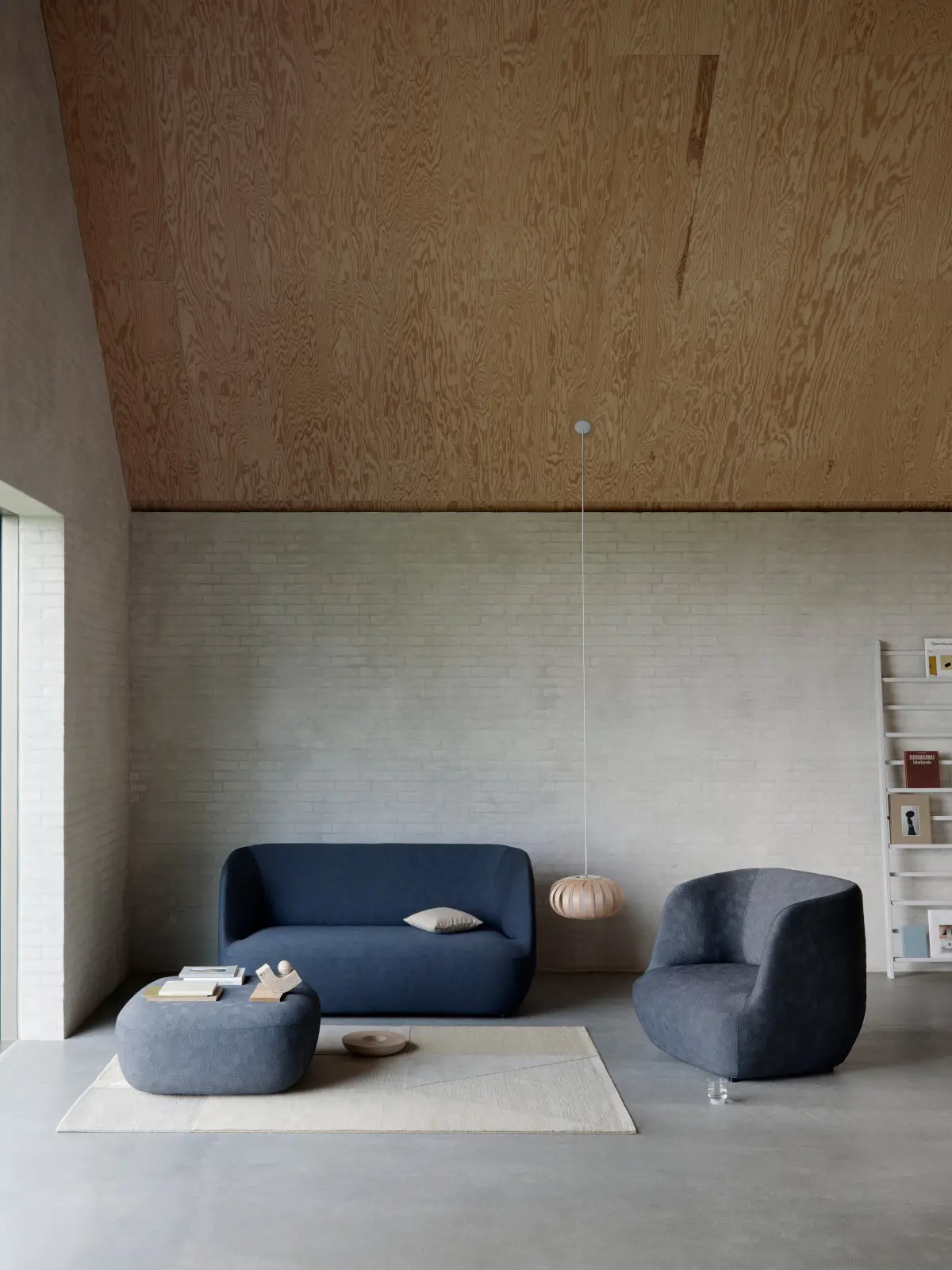 Softline Clay Hocker in Blaugrau vor einem dunkelblauen Sofa und neben einem passenden Sessel in einem modernen Wohnambiente.