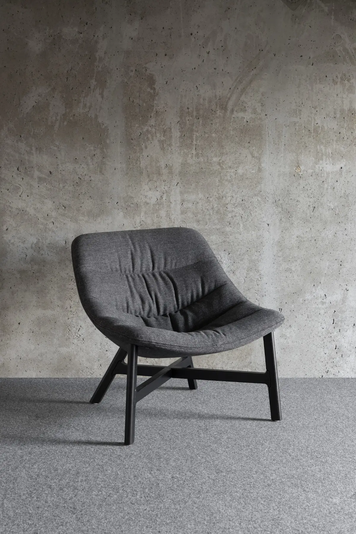 Noti Mishell Soft Sessel in Grau mit Holzbeinen vor moderner Betonwand