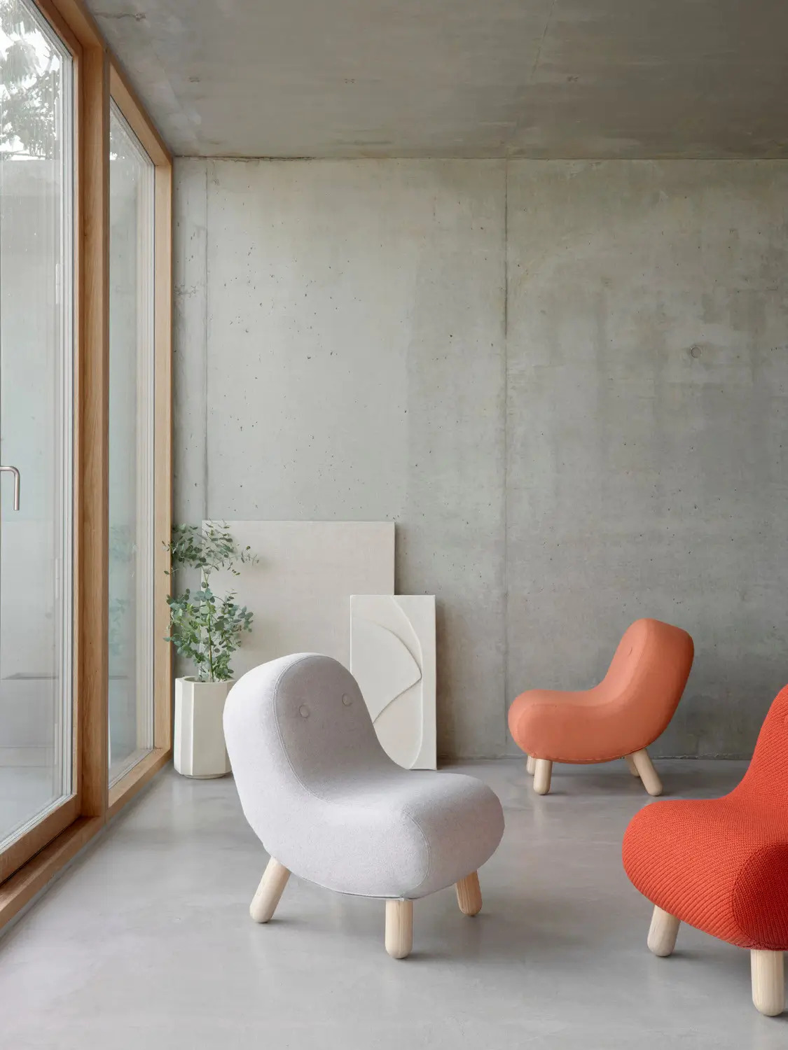 Softline Bob Sessel in Hellgrau, Orange und Rot in einem modernen Wohnambiente mit Betonwand und großen Fenstern.
