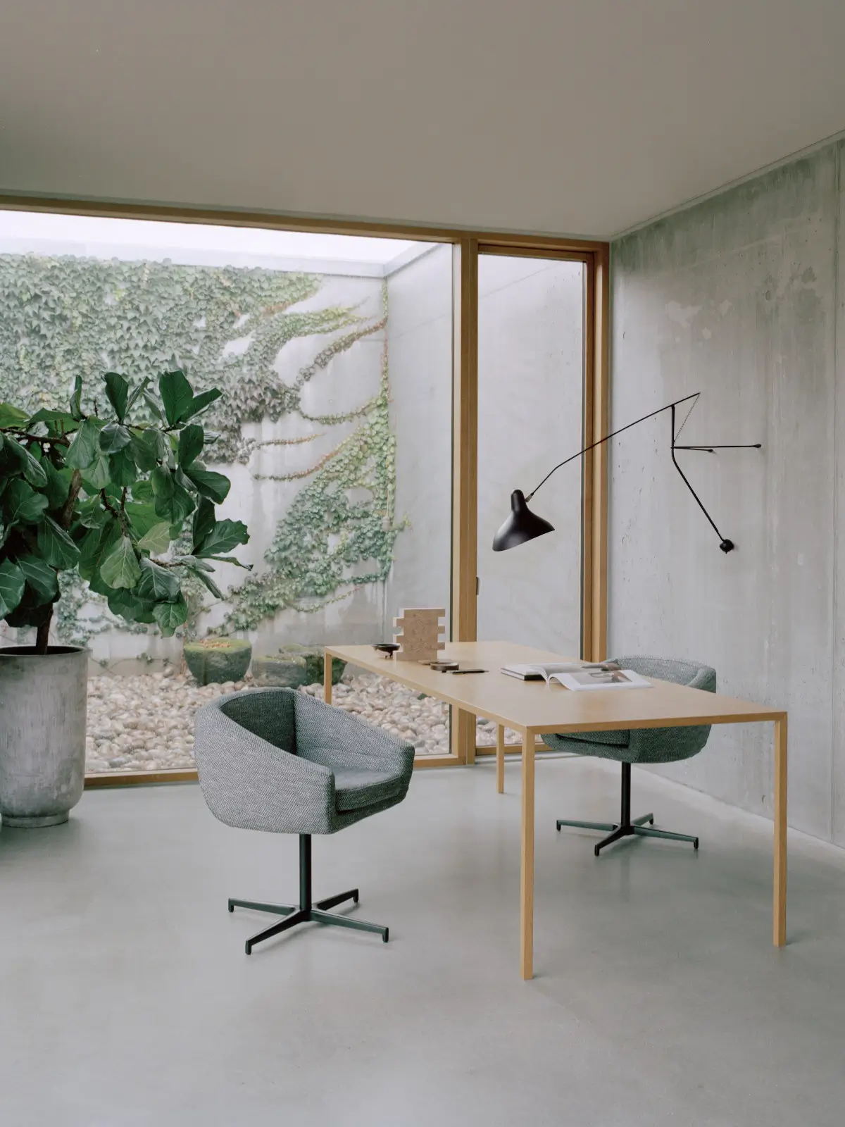 Zwei Softline Aiko Drehsessel in Grau an einem Holztisch in einem modernen Arbeitszimmer mit großen Fenstern und grünen Pflanzen.