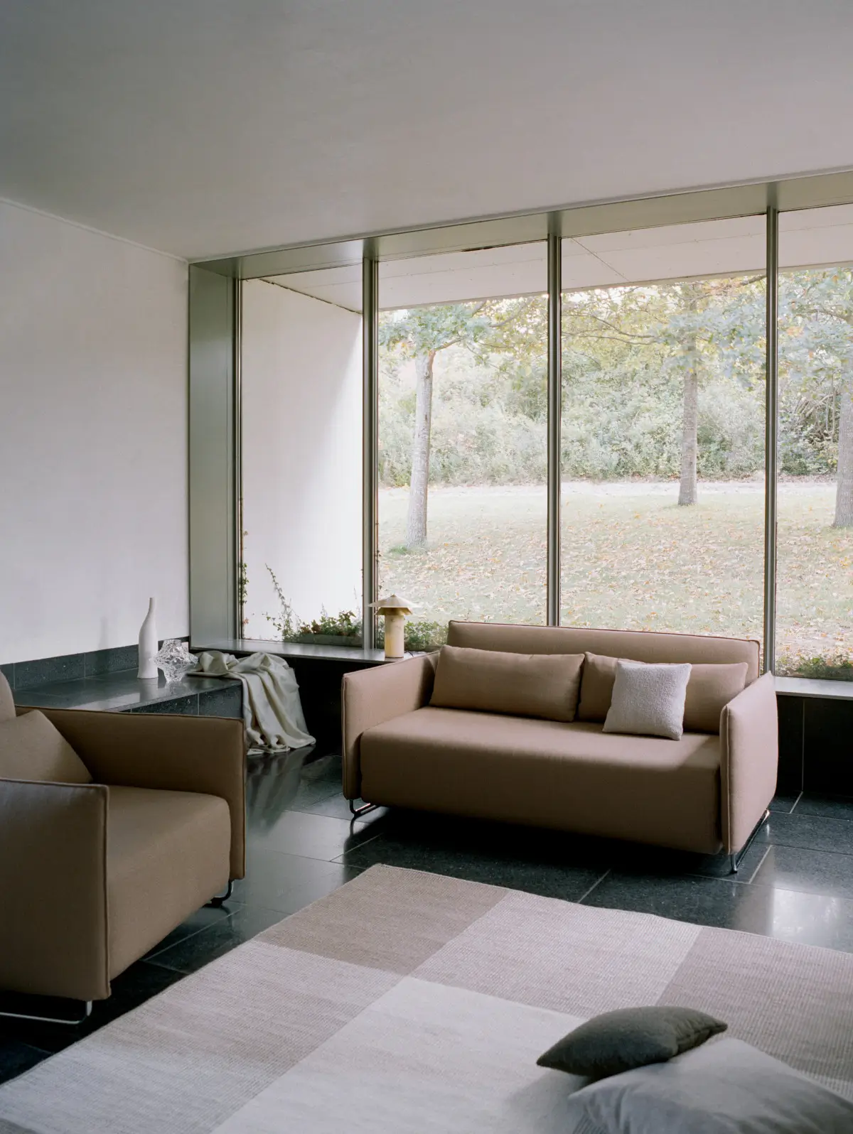 Softline Cord Sessel in Beige zusammen mit passendem Sofa in einem hellen Wohnambiente mit großen Fenstern, dunklem Fliesenboden und Teppich.