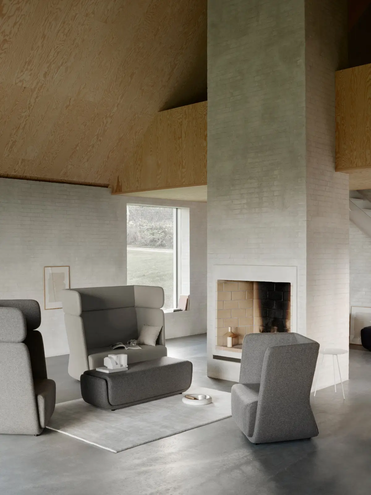 Softline Basket Sessel in Grau in einem modernen Wohnzimmer mit weiteren gepolsterten Sitzmöbeln, Hocker, Teppich und Kamin.