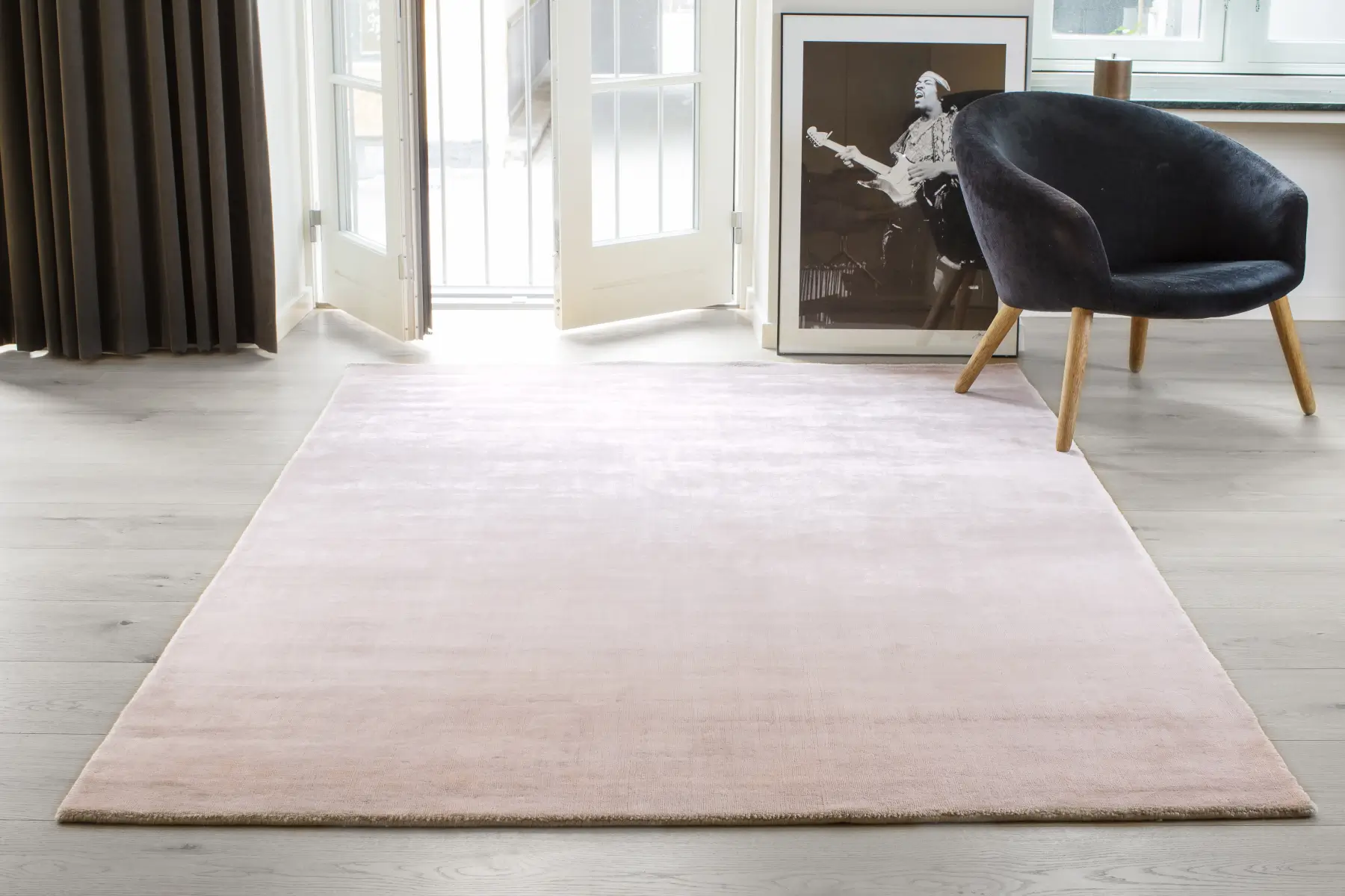 Massimo Copenhagen Bamboo Teppich in zartem Rosa auf hellem Holzboden in einem modernen Wohnraum mit dunklem Polstersessel und großen Fenstertüren.