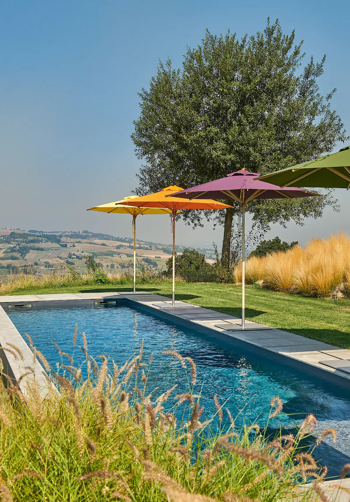 Mehrere Weishäupl Klassiker Schirme Ø 190 cm in verschiedenen Farben am Pool in hochwertiger Gartenlandschaft