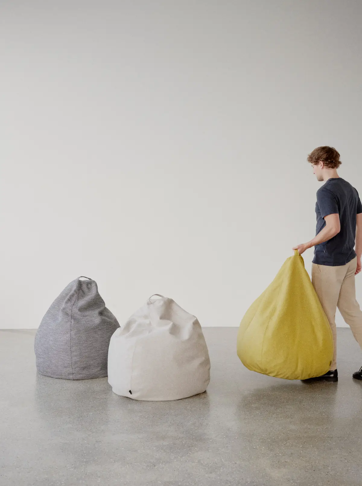 Softline Esprit Sitzsäcke in Grau, Hellgrau und Gelb; der gelbe Sitzsack wird am integrierten Tragegriff angehoben und zeigt die flexible Form.