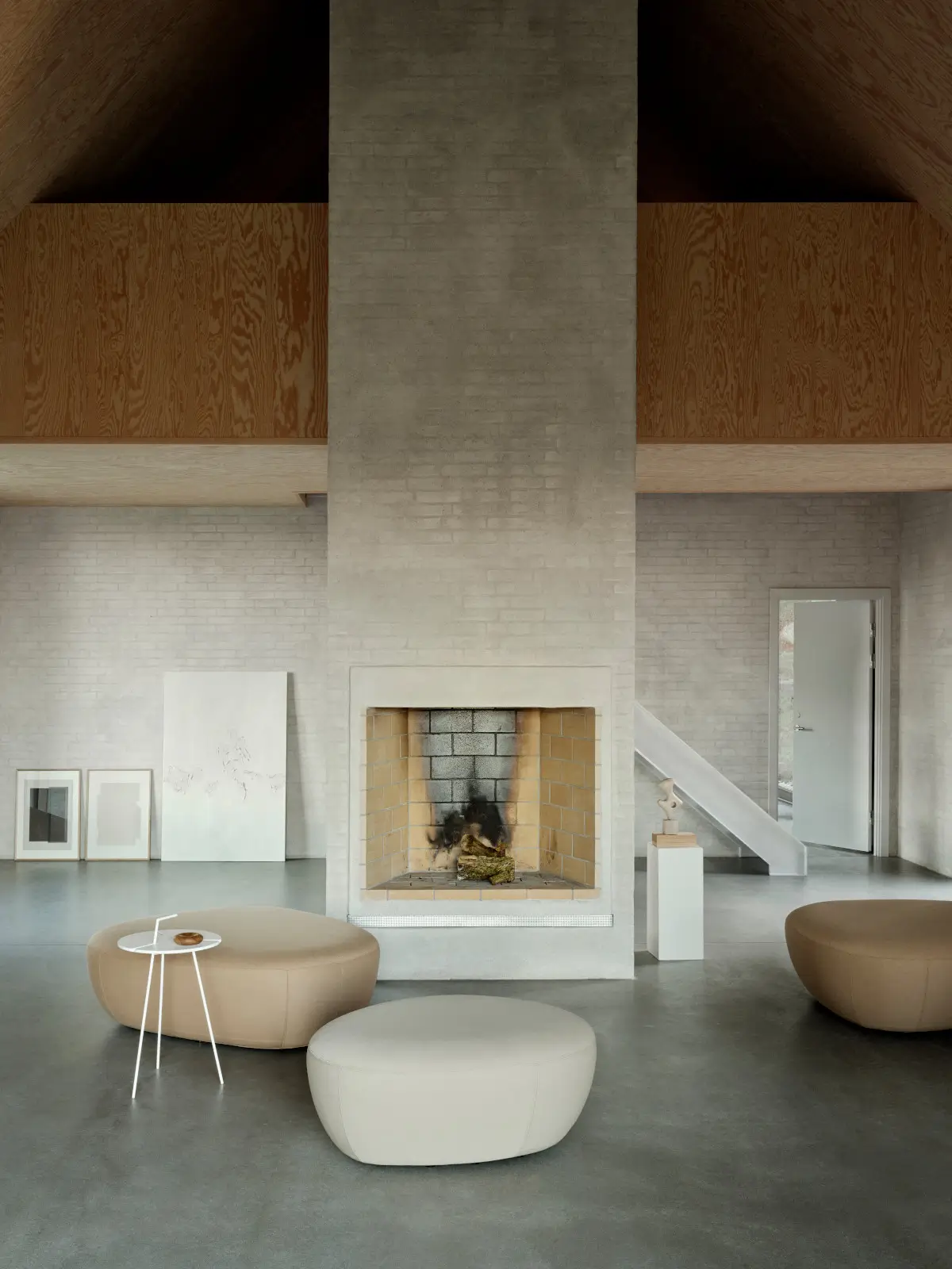 Softline Sisters Hocker Small in Beige und Hellgrau in einem modernen Wohnambiente vor einem großen Kamin mit hohen Decken und Holzelementen.
