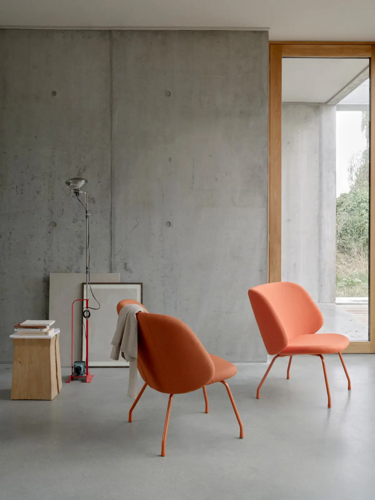 Zwei Softline Evy Sessel in Orange mit farblich abgestimmtem Metallgestell in einem modernen Wohnambiente mit Betonwand und großem Fenster.