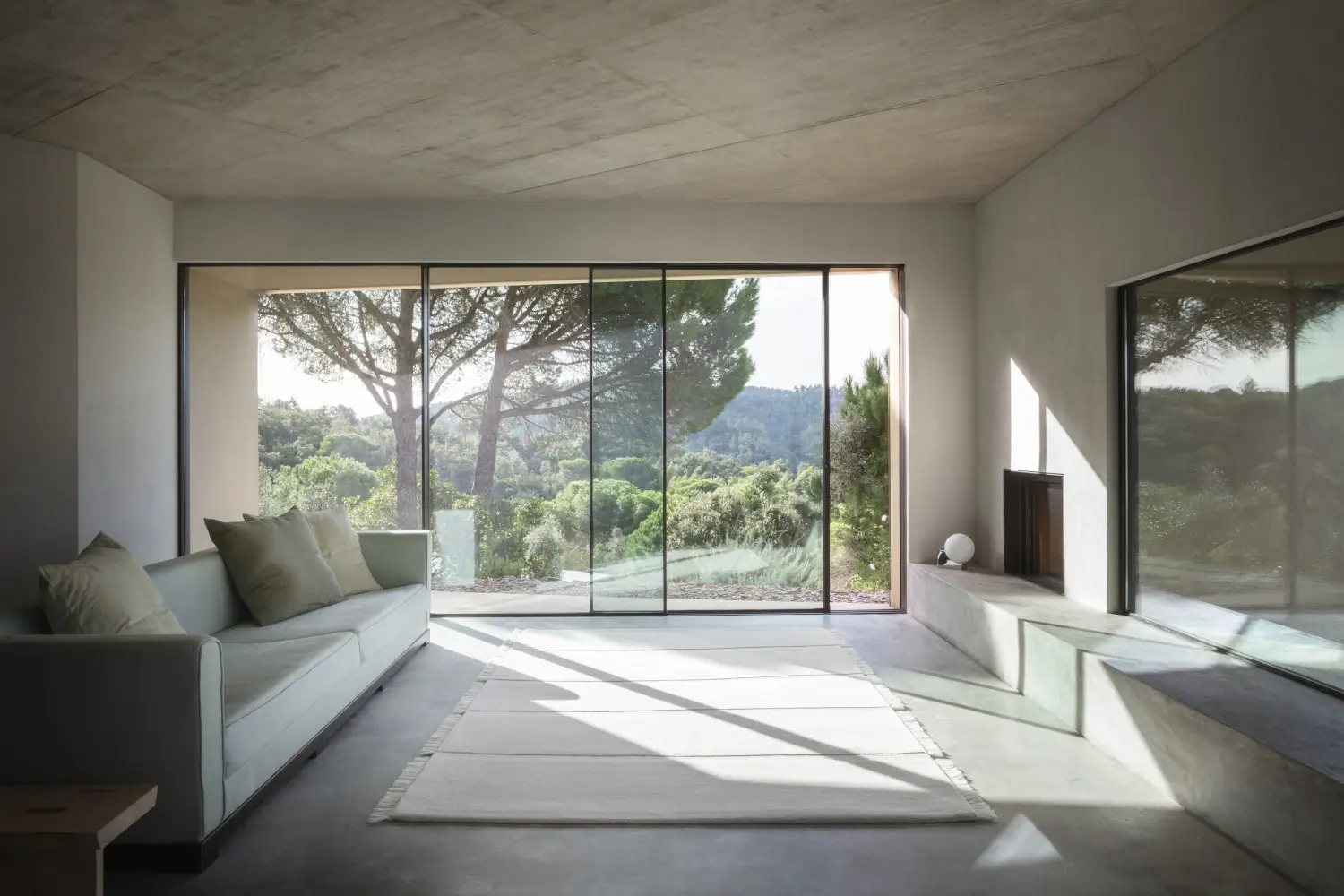 Massimo Copenhagen Atoll Teppich in Cream mit schmalen Querstreifen und Fransen vor einem hellen Sofa in einem großzügigen Wohnzimmer mit Panoramaverglasung.