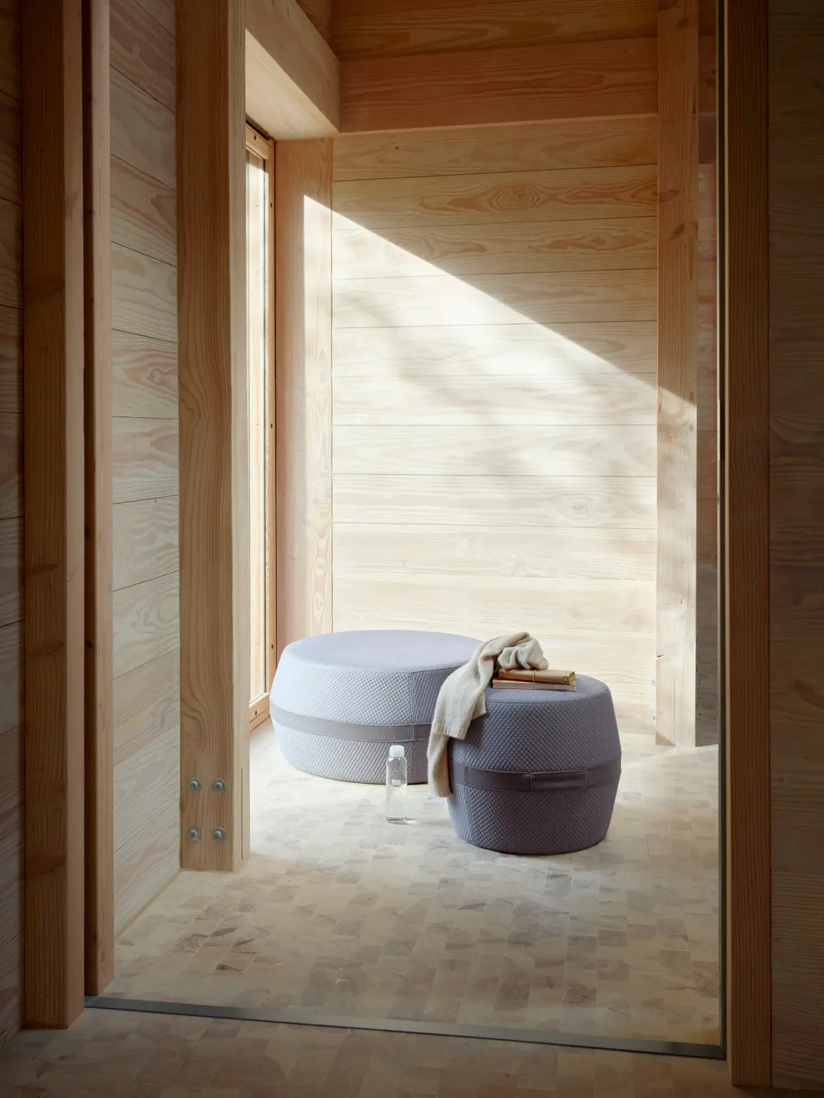 Softline Lisbon Hocker in zwei Größen und Grautönen in einem hellen Wohnambiente mit Holzwänden und natürlichem Lichteinfall.