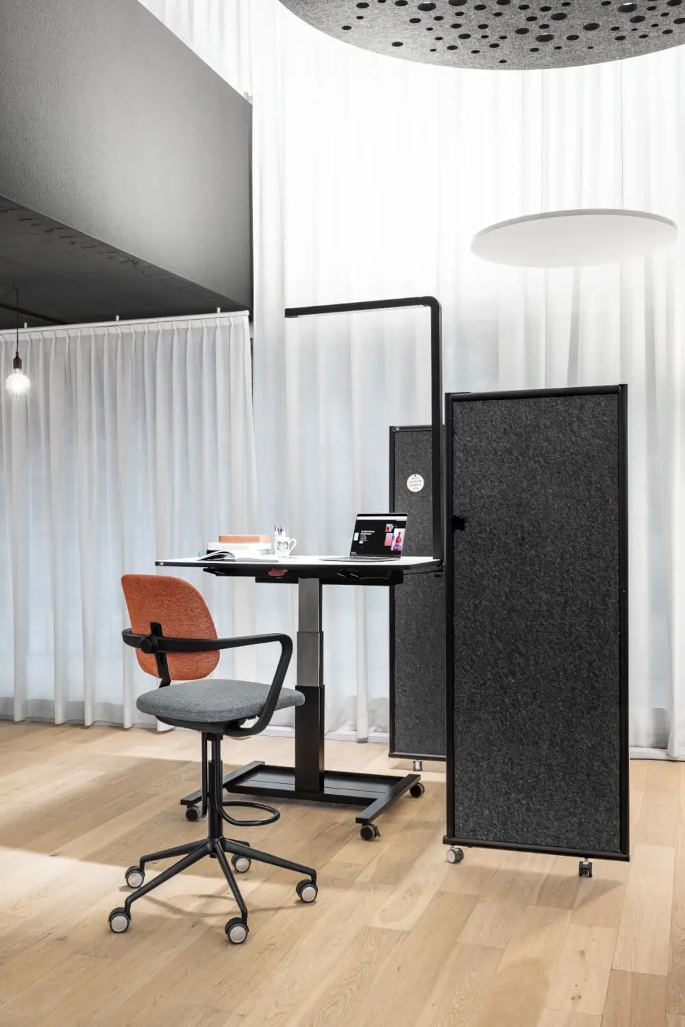 Girsberger Ategra Bürostuhl an einem höhenverstellbaren Schreibtisch mit Akustikpaneelen im modernen Büro.
