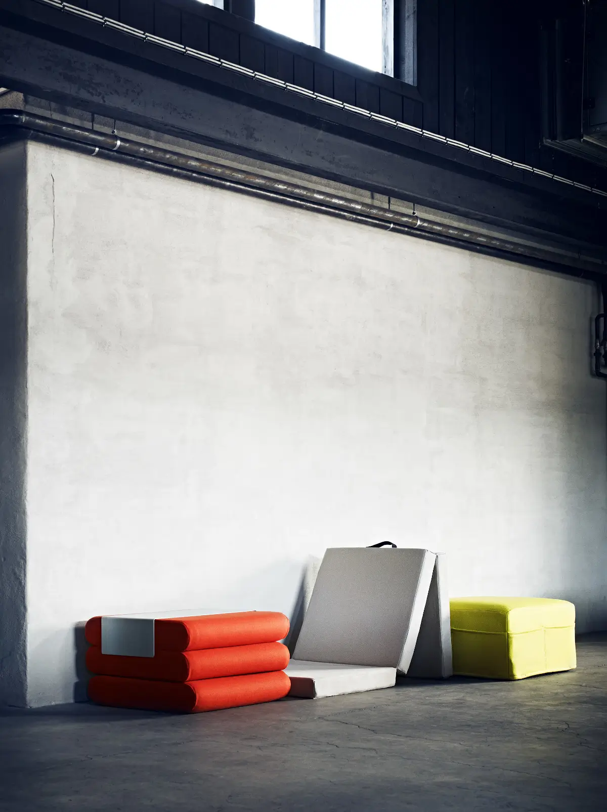 Softline Bingo Hocker in Orange und Gelb sowie ein ausgeklapptes helles Modell in einem industriell gestalteten Innenraum.