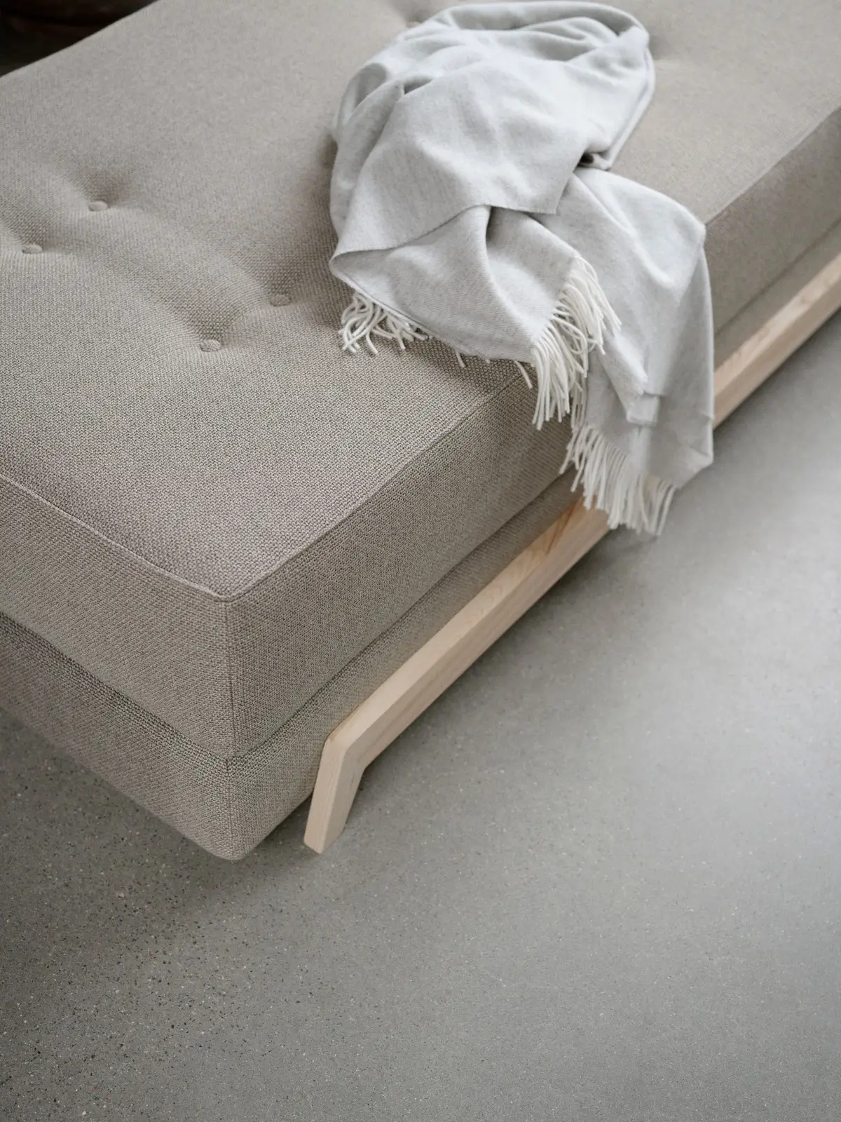 Softline Frame Daybed in Beige in detaillierter Nahansicht mit gepolsterter Liegefläche, Knopfheftung, hellem Holzgestell und aufgelegter Decke.