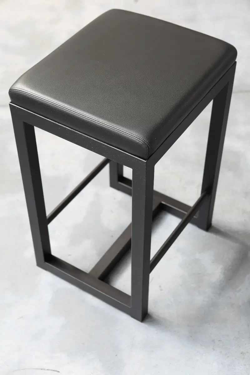 Zeus Big Brother Barhocker in Schwarz aus Stahl mit gepolsterter Sitzfläche in einer Schrägansicht bei 64 cm Höhe.