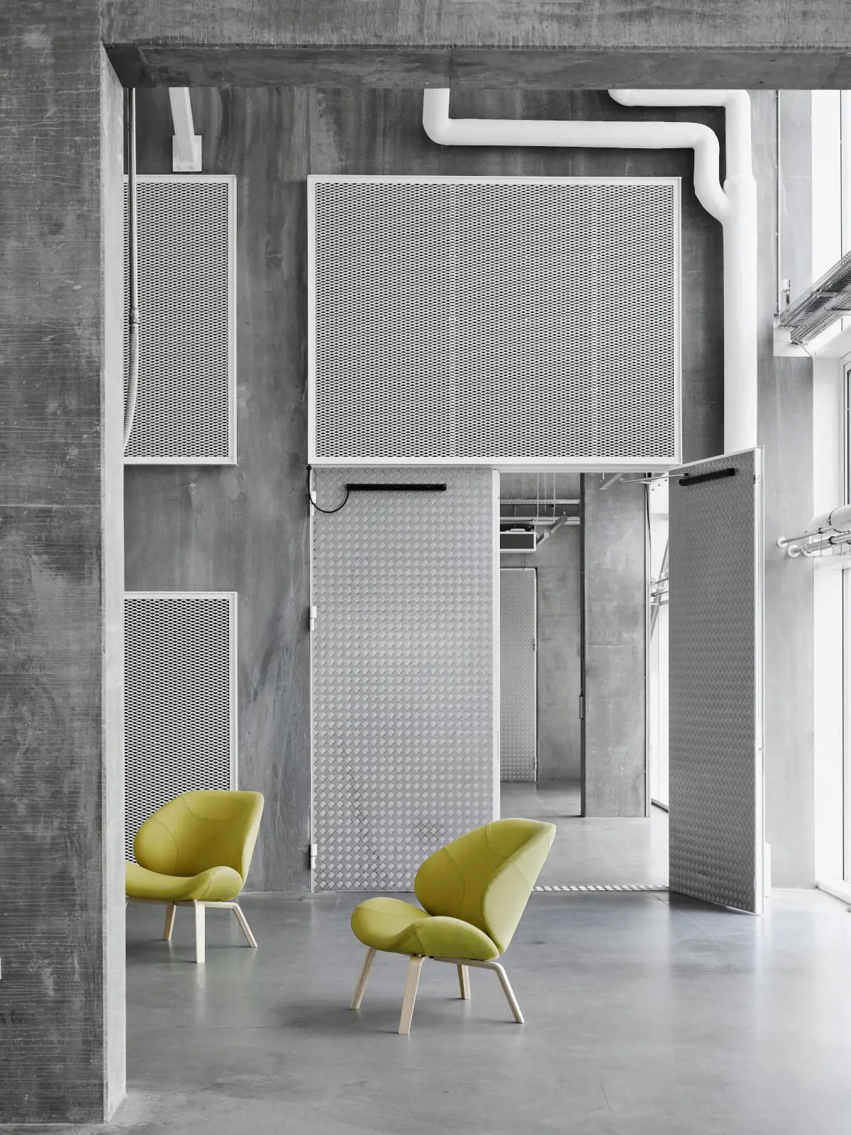 Zwei Softline Eden Sessel in Grün mit hellem Holzgestell in einem modernen, offen gestalteten Industrieambiente.