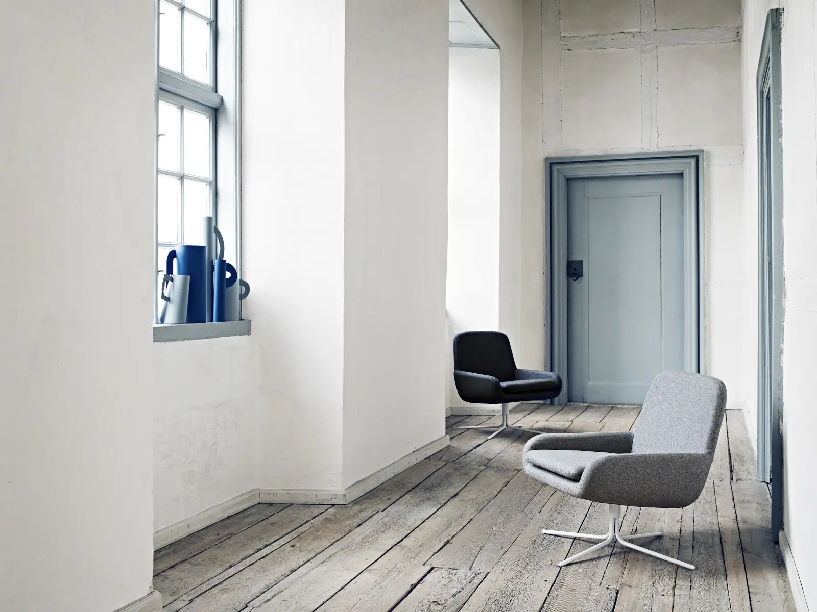 Zwei Softline Coco Drehstühle in Grau und Anthrazit in einem hellen Wohnambiente mit Holzboden, hohen Fenstern und weißen Wänden.