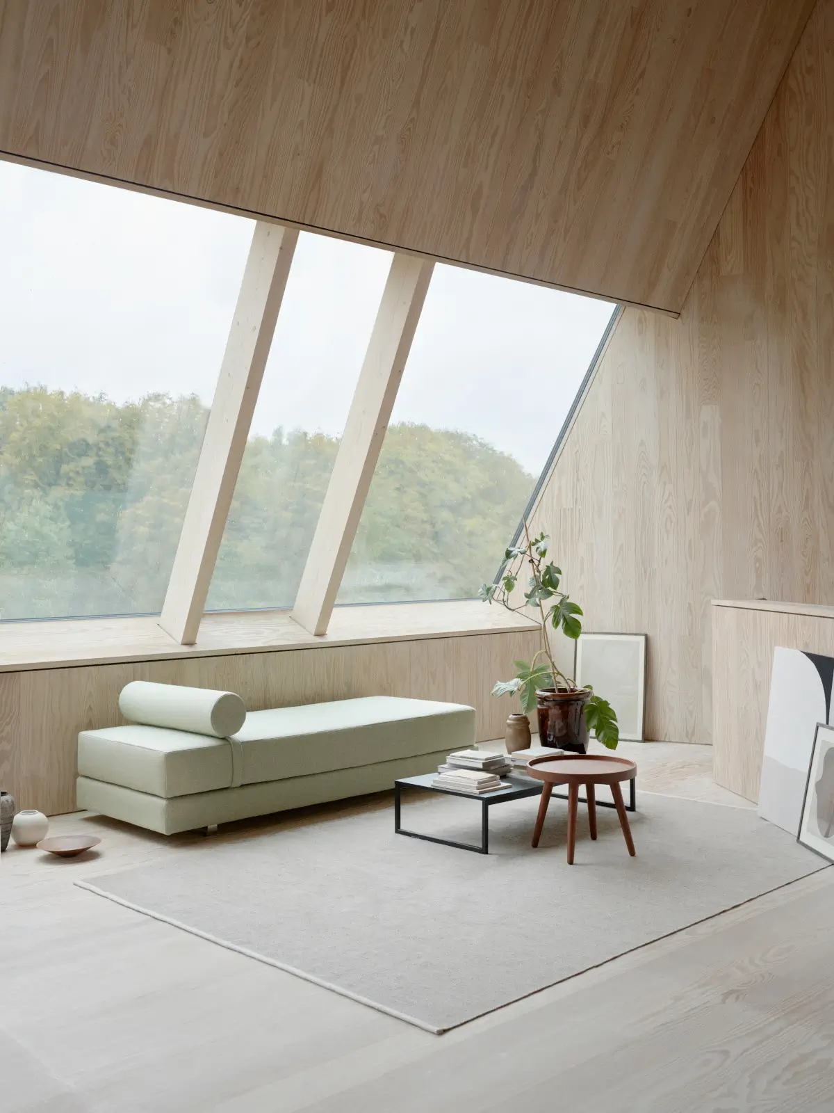 Softline Lubi Daybed in Hellgrün aus seitlicher Perspektive mit gepolsterter Liegefläche und rundem Nackenpolster in einem hellen Wohnambiente mit Holzverkleidung.